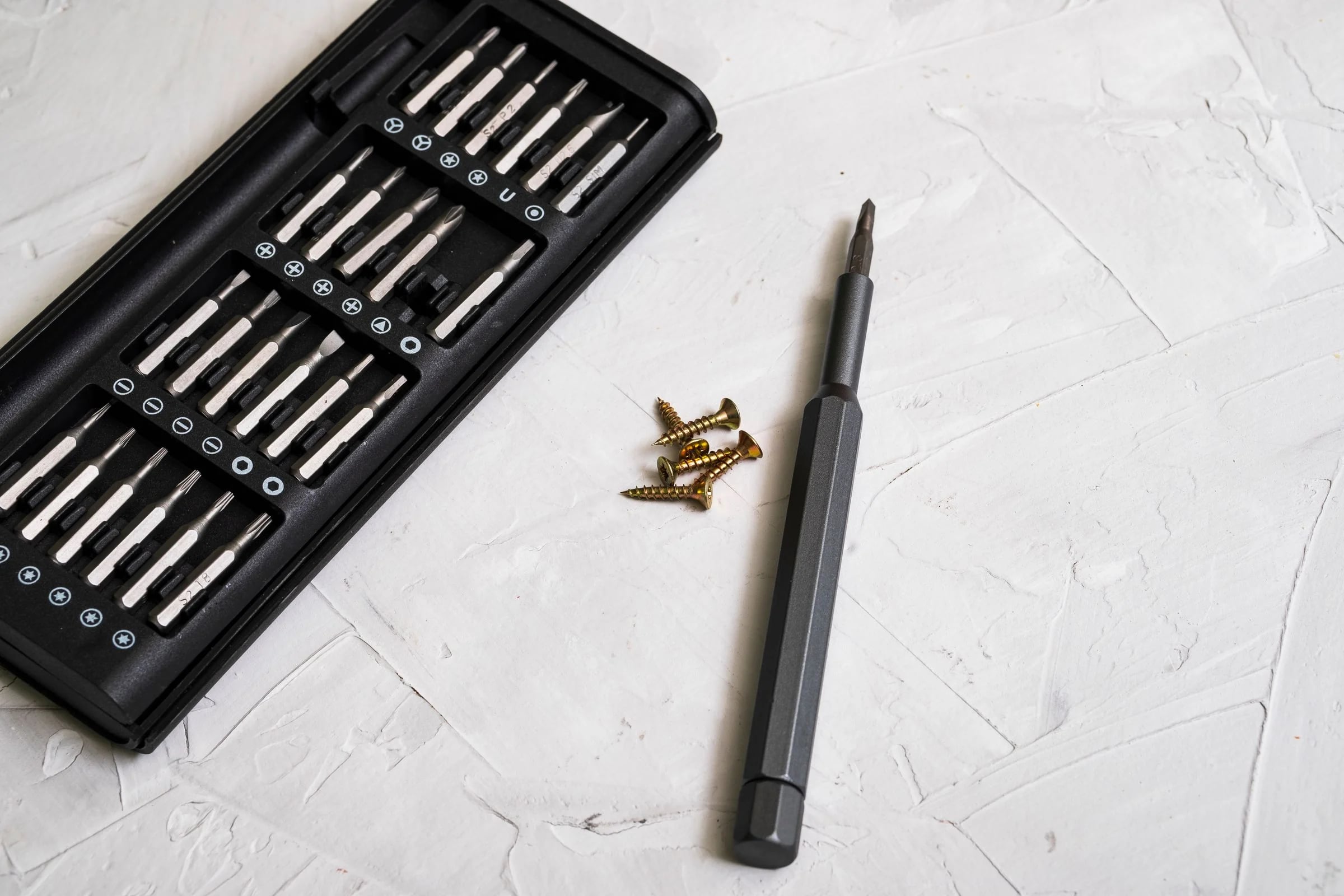 Estuche de puntas de precisión y destornillador junto a unos tornillos sobre una mesa blanca