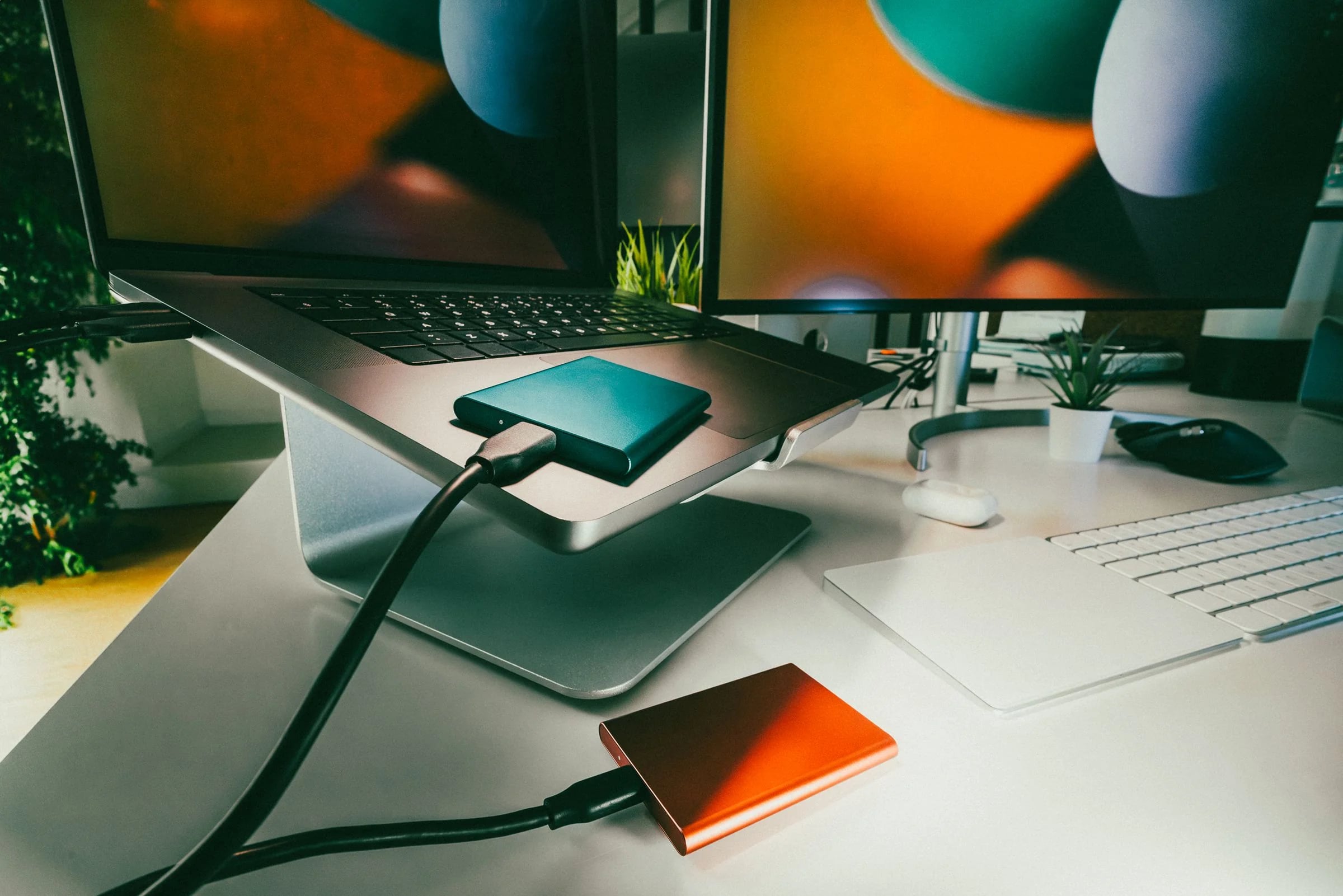 Dos discos externos conectados a un portátil sobre soporte en un escritorio de oficina con monitor