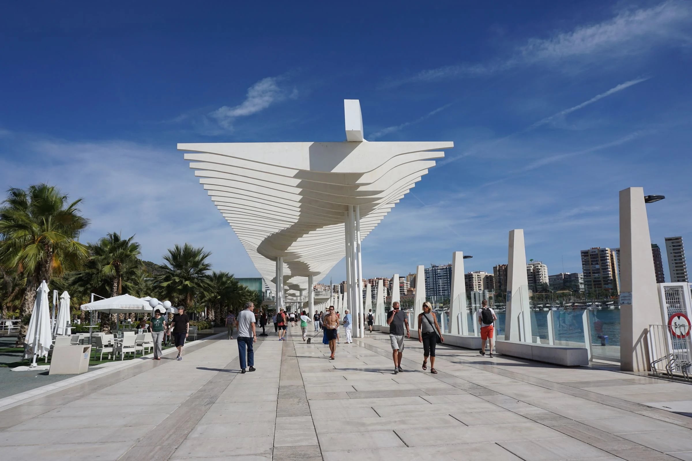 Paseo del Muelle Uno de Málaga con su pérgola blanca, palmeras y paseantes