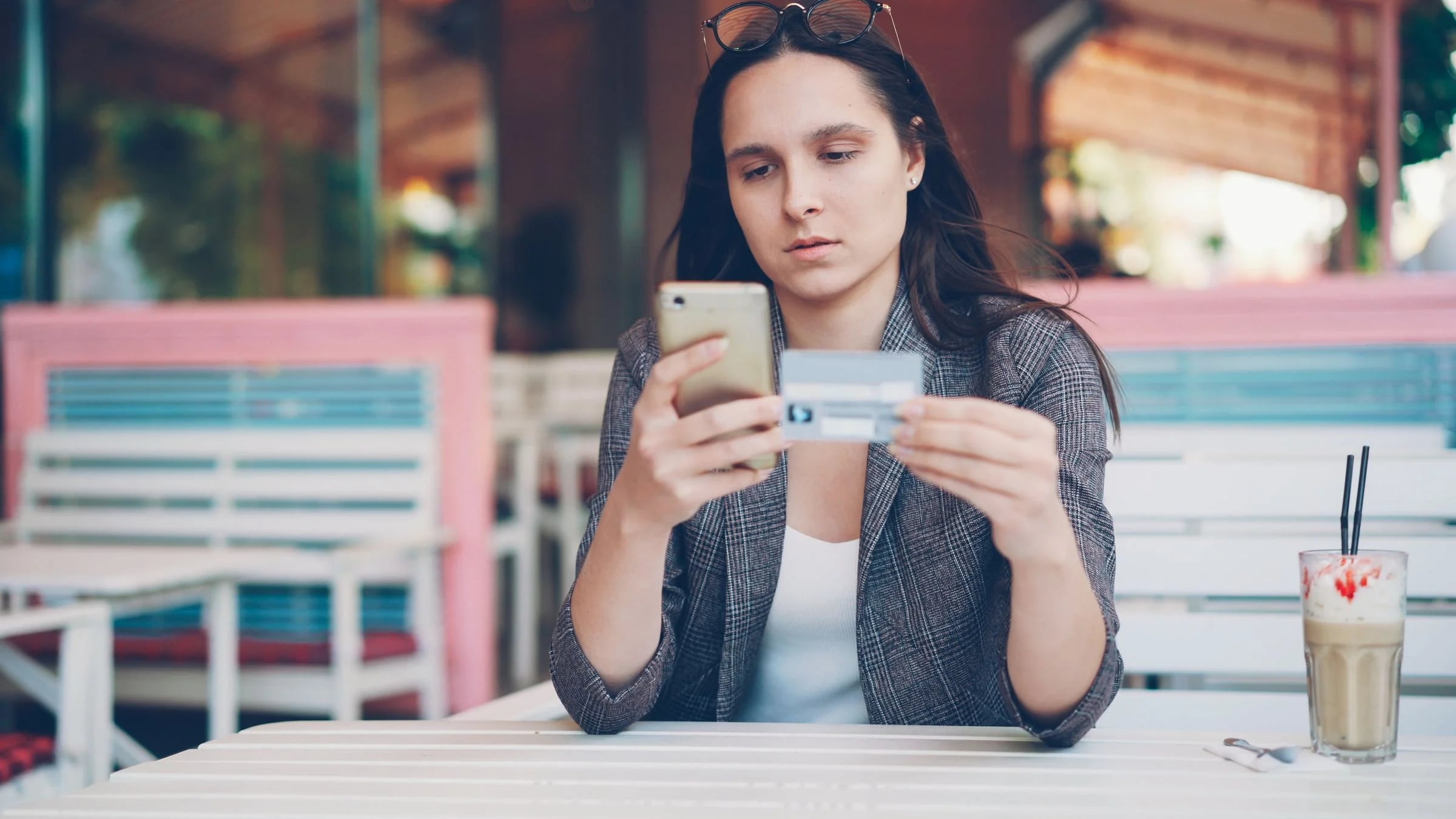 Mujer paga una compra por internet con el móvil y la tarjeta en la terraza de una cafetería