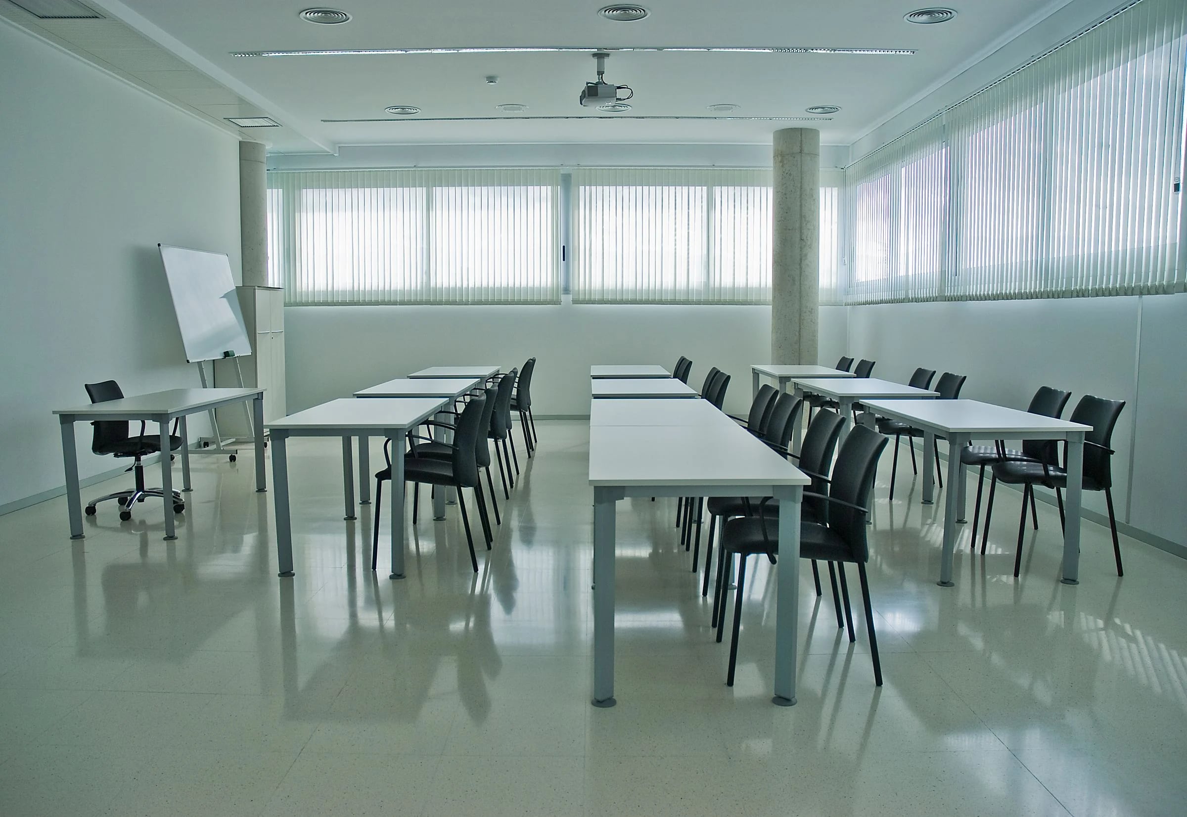 Aula de formación vacía con mesas en filas, pizarra y proyector