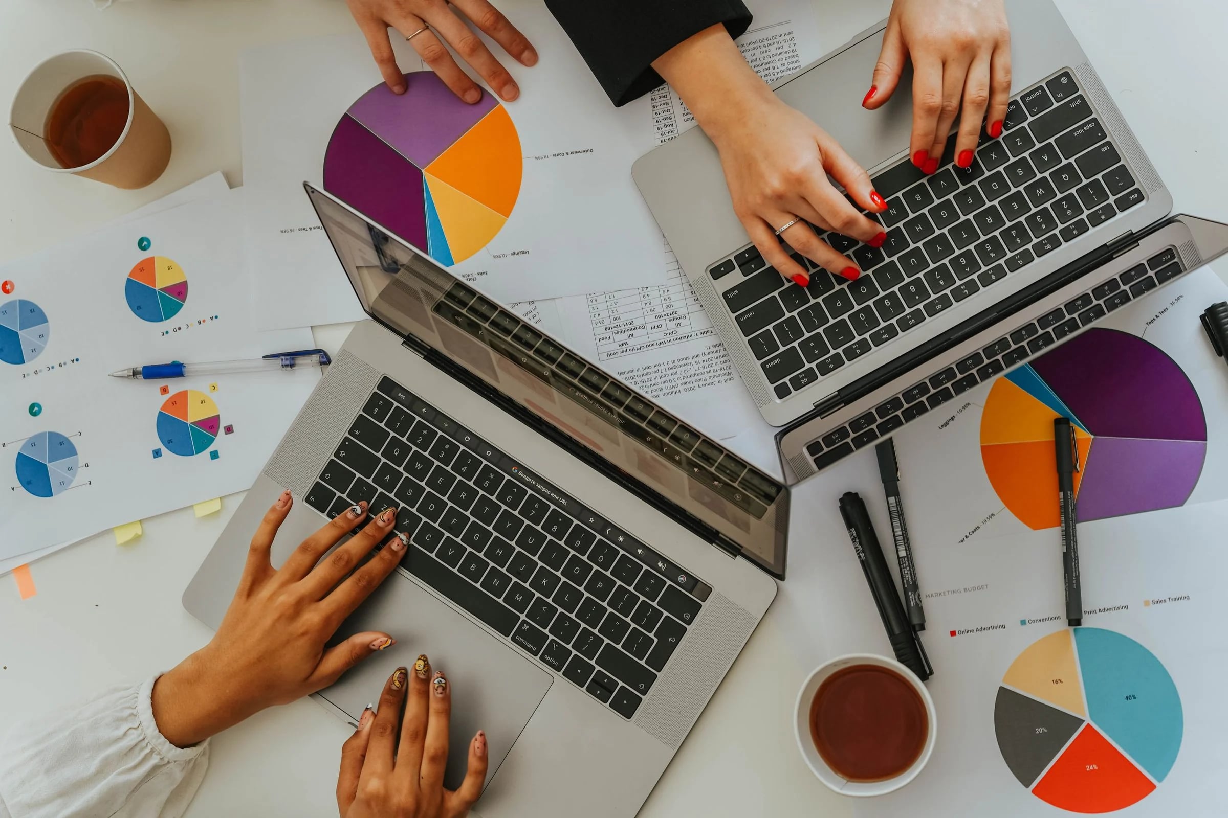 Vista cenital de tres personas trabajando con portátiles entre informes con gráficos circulares