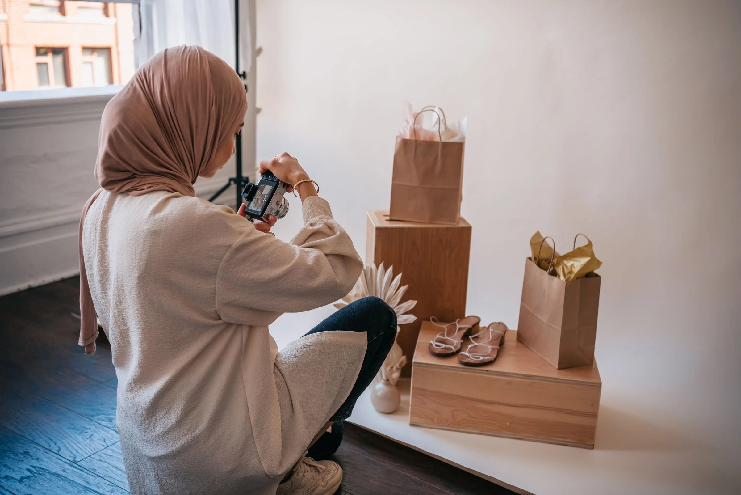 Emprendedora con hiyab fotografía sandalias y bolsas sobre peanas de madera para su tienda online