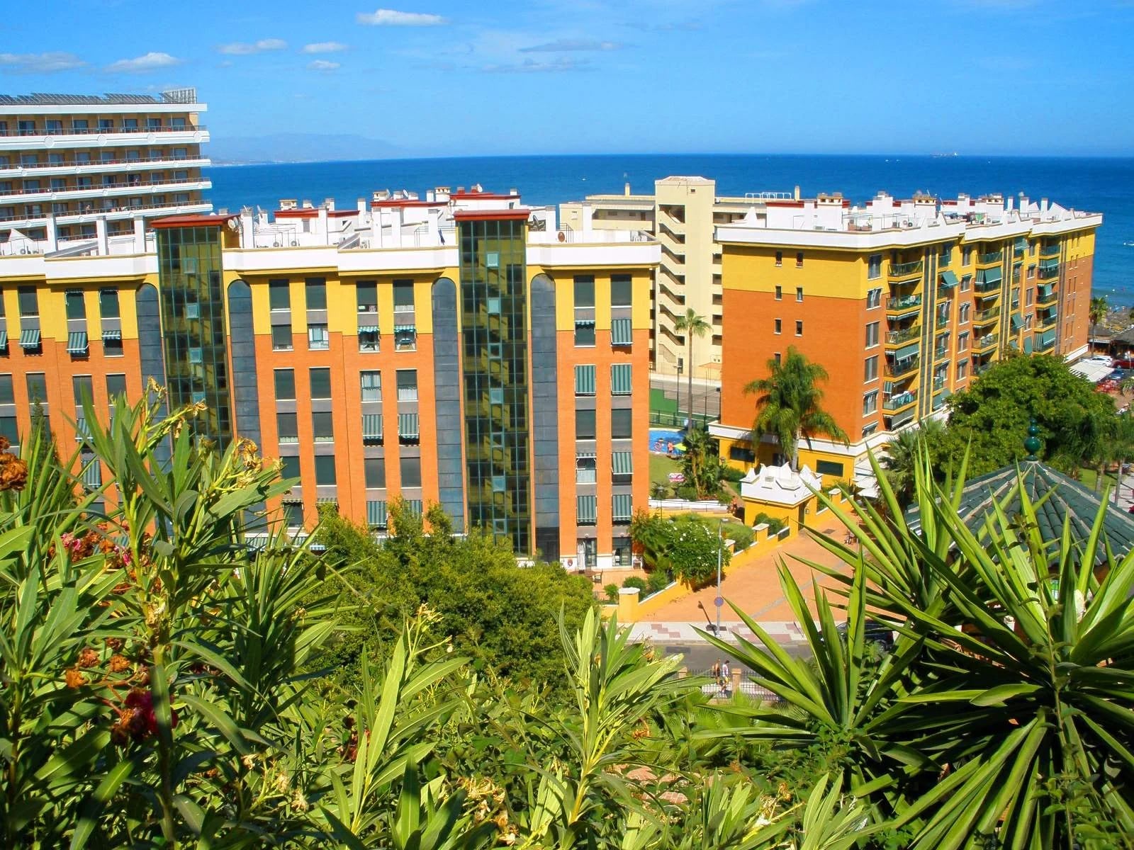 Bloques de apartamentos de colores en Torremolinos entre vegetación, con el mar al fondo